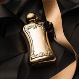 Parfums de Marly Darcy gouden parfumfles ligt in een doos met zwart vloeipapier met een gouden lint ernaast